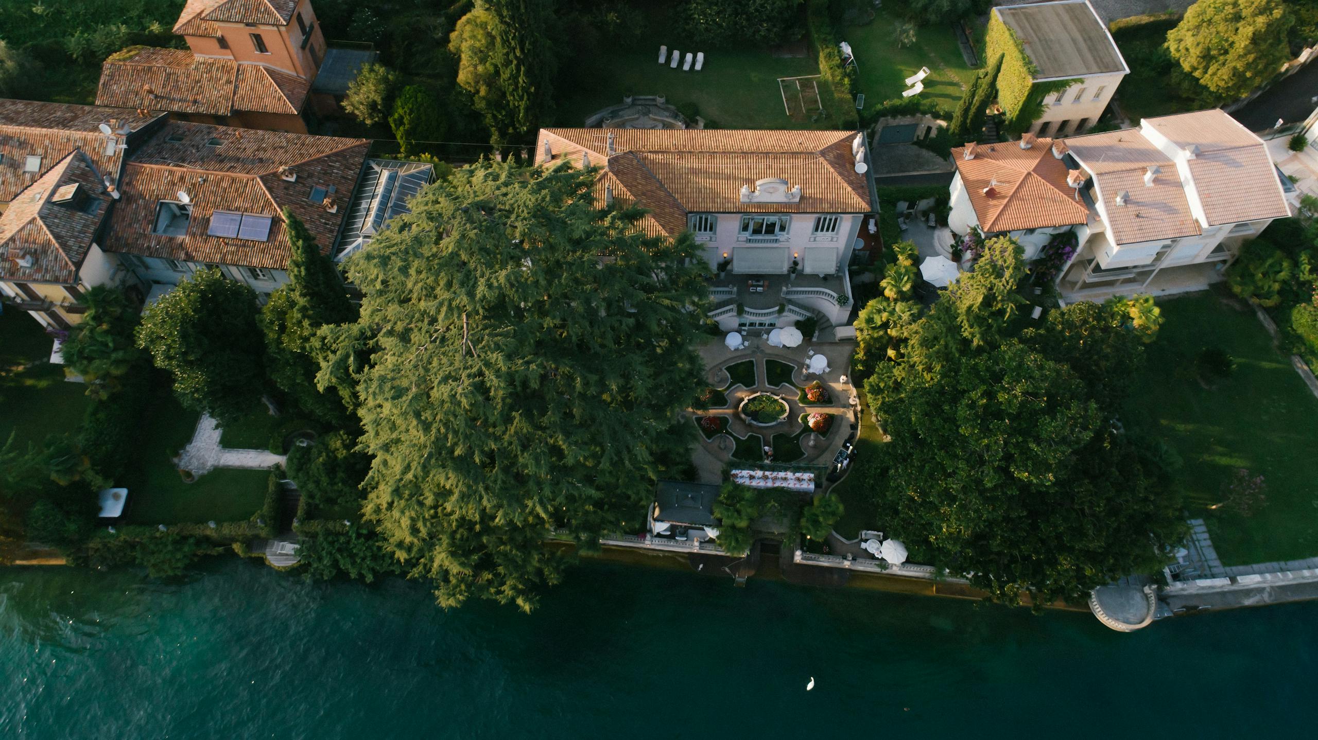 Stunning aerial view of elegant lakeside mansions surrounded by lush gardens and clear waters.